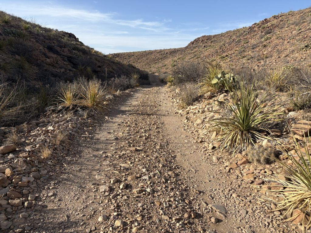 A dirt road leading into a desert valley with rocky hills in the background.