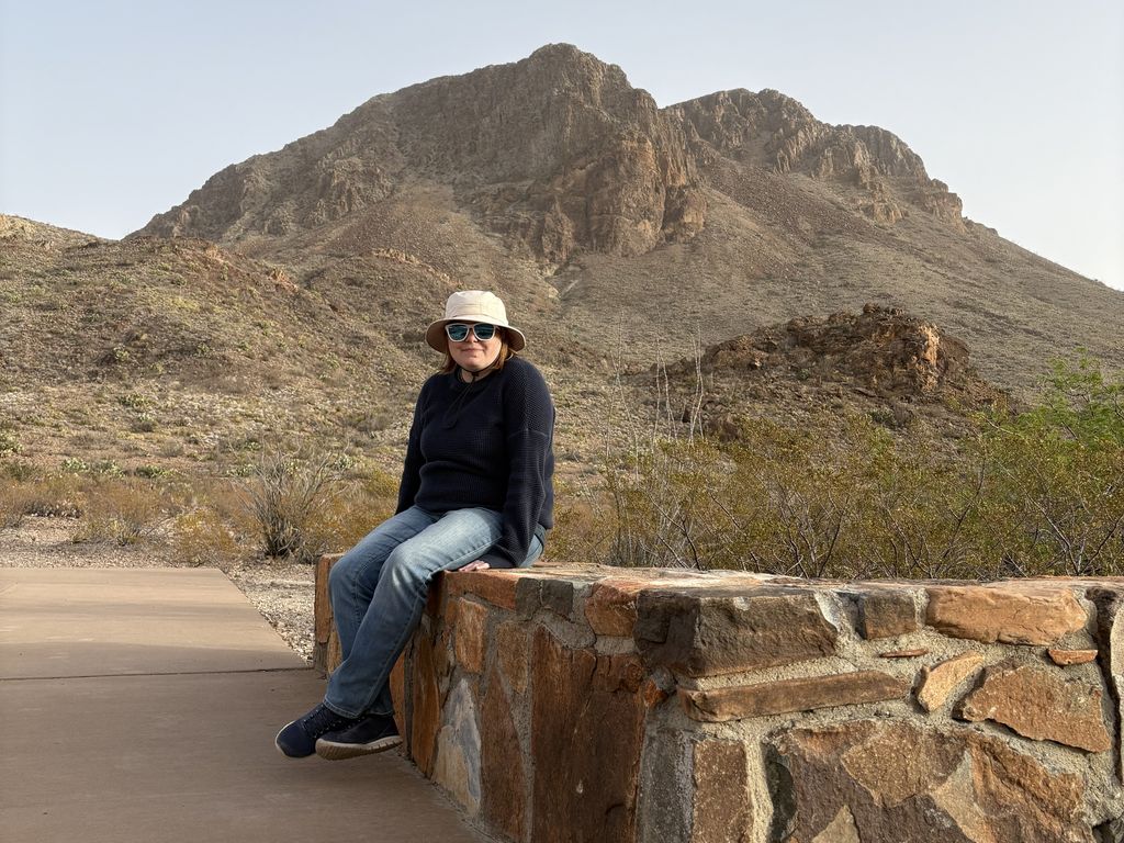 Caitlin sitting on a stone wall with a desert mountain peak in the background.