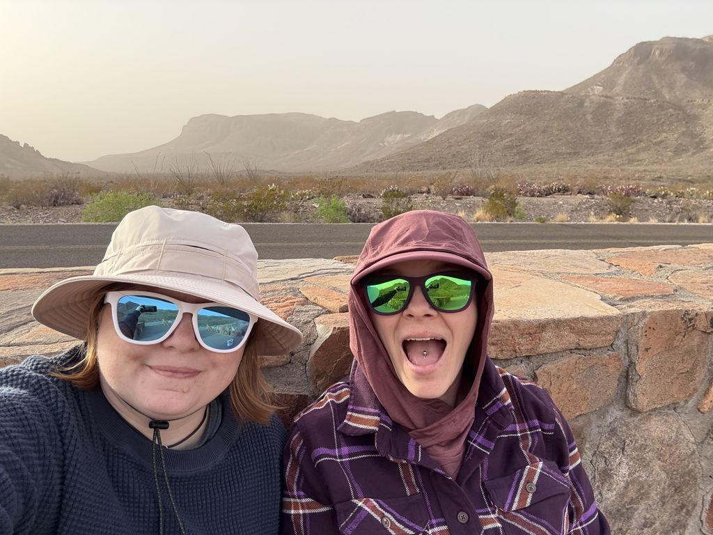 Caitlin and Scout wearing sunglasses and smiling in front of desert mountains.